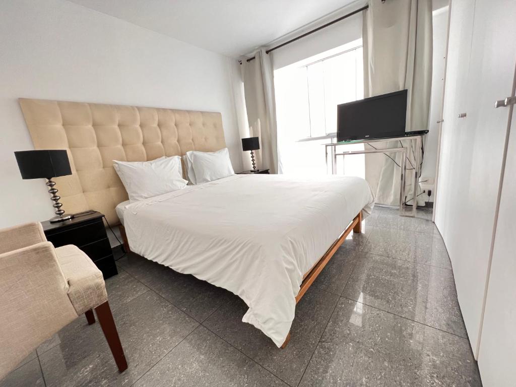 1 dormitorio con 1 cama blanca grande y TV en Apartamento en Miraflores La paz, en Lima
