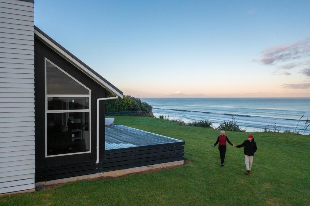 2 personnes marchant sur le côté d'une maison dans l'établissement MOKAU BEACH HOUSE, à Mokau