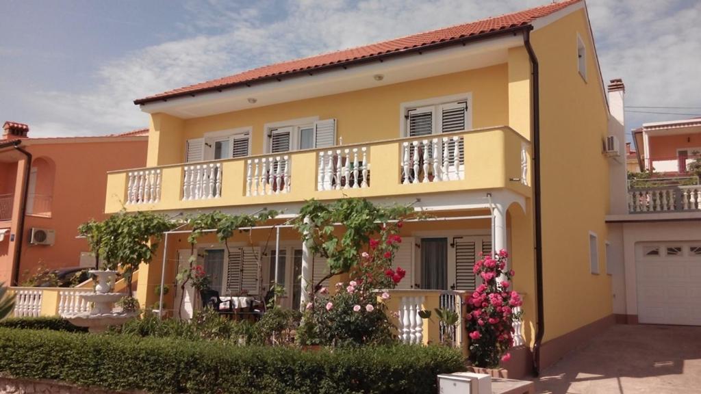 a yellow house with a balcony and flowers at Apartment and room Hudoletnjak in Šilo