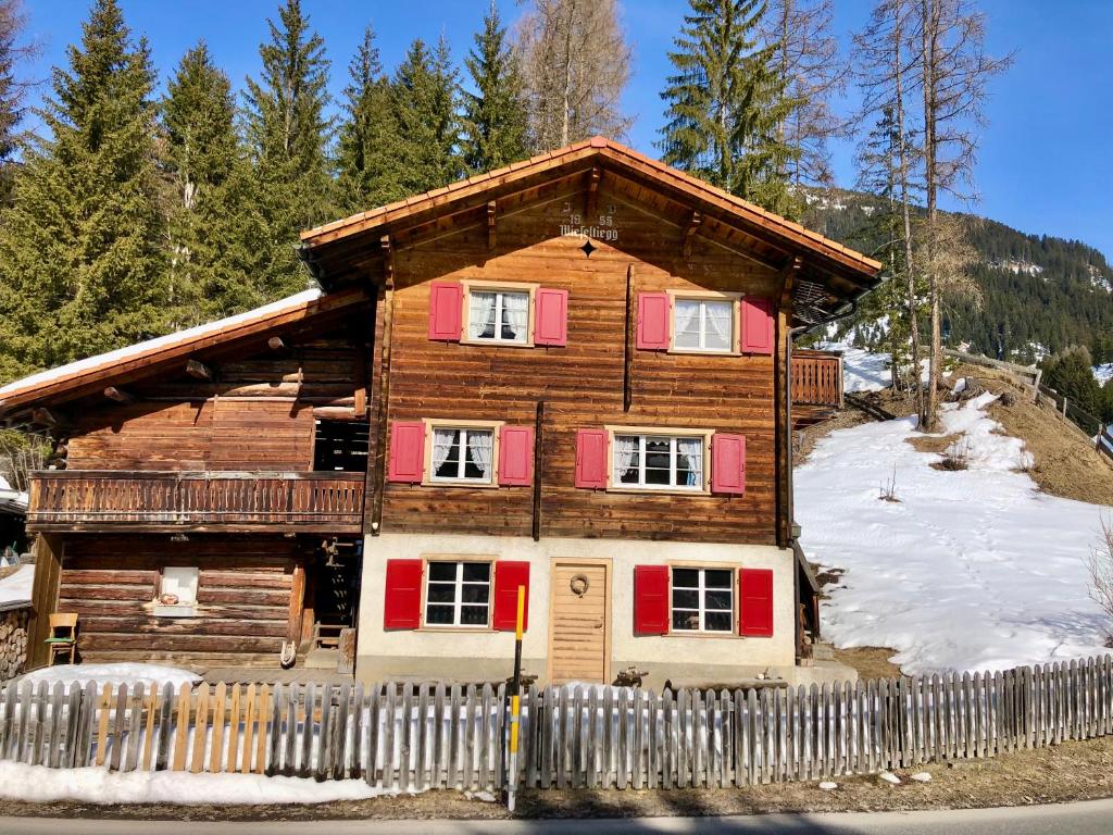 una casa de madera con persianas rojas en la nieve en Charming Chalet with mountain view near Arosa for 6 People house exclusive use, en Langwies