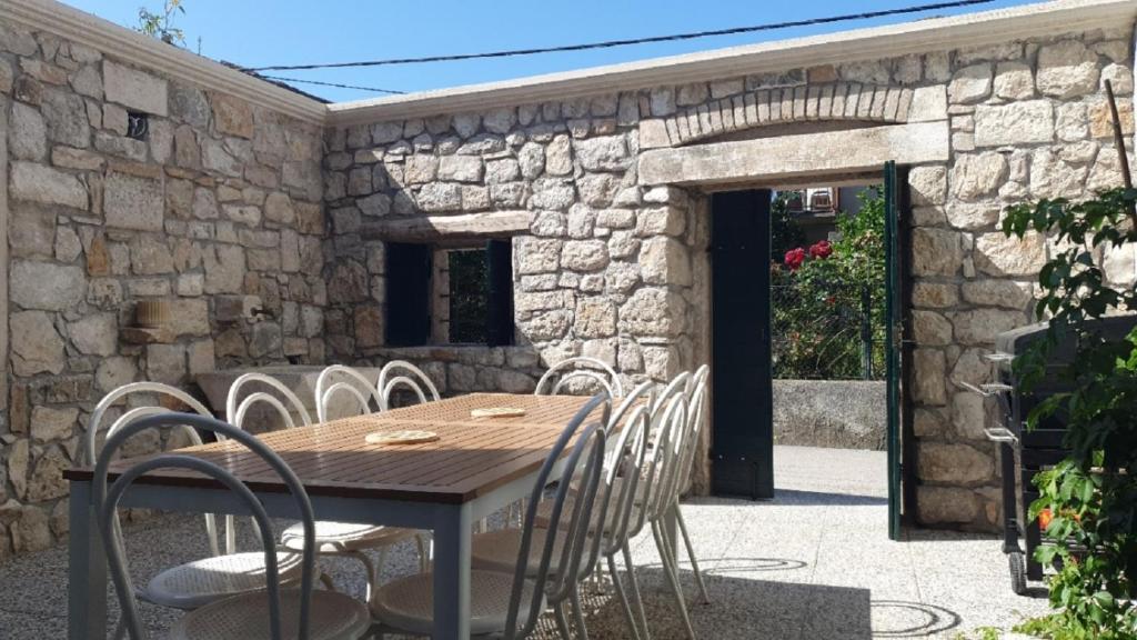 um pátio com paredes de pedra, uma mesa e cadeiras de madeira em Holiday house - Dvori Vlahovici em Opuzen