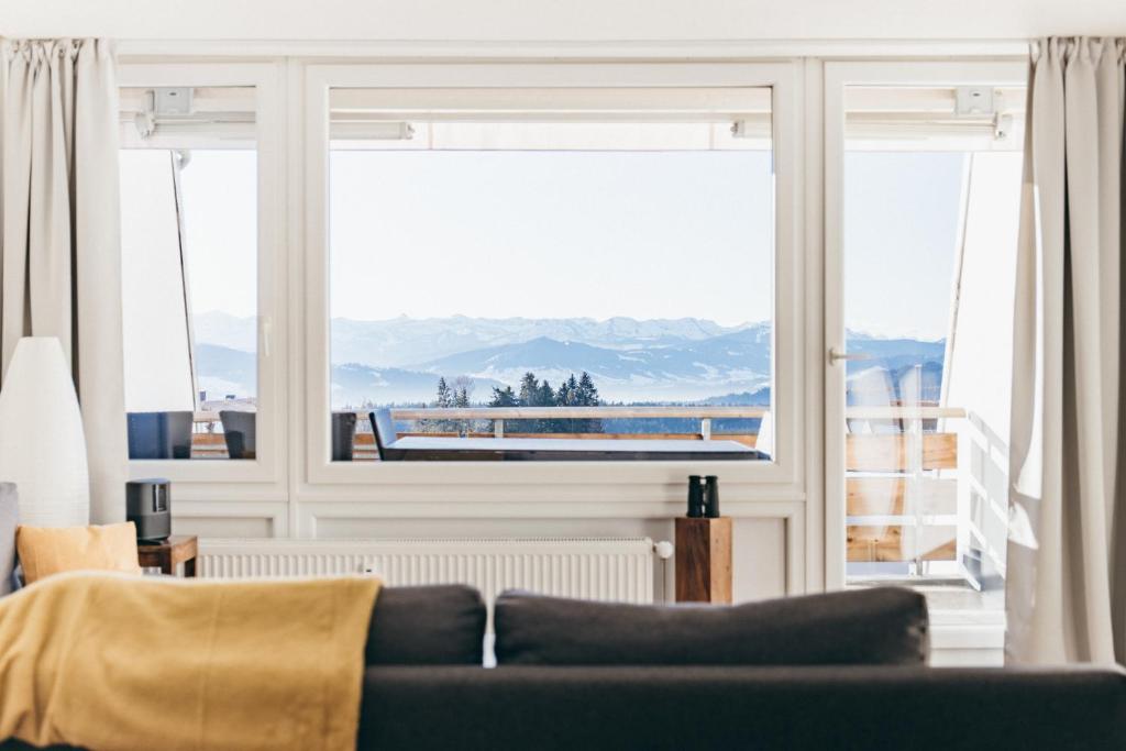 uma sala de estar com um sofá e uma grande janela em HEIMATEL - Ferienwohnungen em Scheidegg