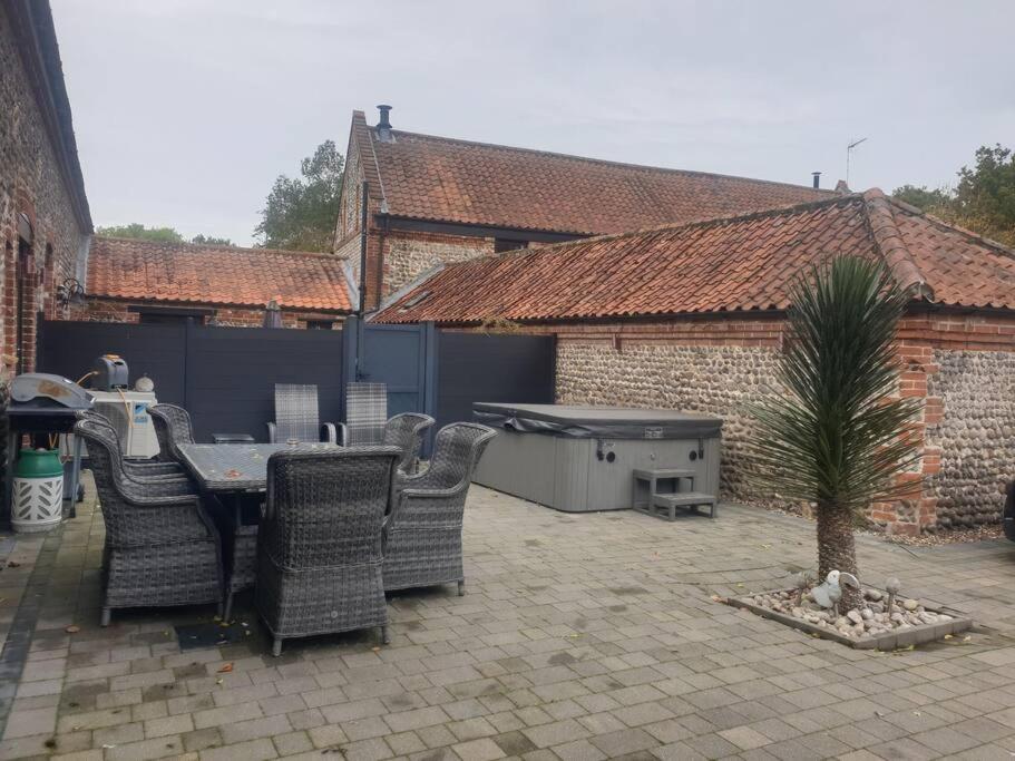 a patio with a table and chairs and a palm tree at Luxury barn with hot tub (Dogs Welcome) in Roughton