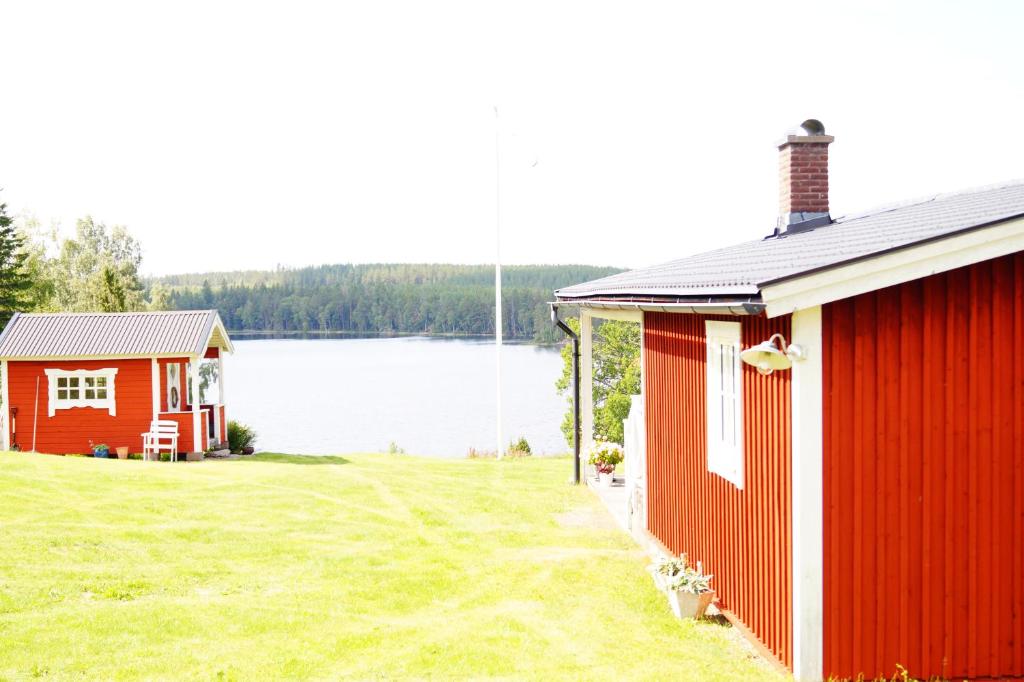 two red buildings with a lake in the background at Stuga med sjöutsikt. in Ingatorp