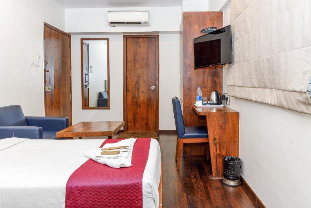 a hotel room with a bed and a desk and a tv at J Hotel and Banquets in Mumbai