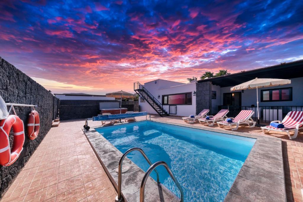 a swimming pool with chairs and a sunset at Villa Aurelia - Pool, Jacuzzi, BBQ and Ping-Pong By Lanzarote Vacation Homes in Playa Blanca