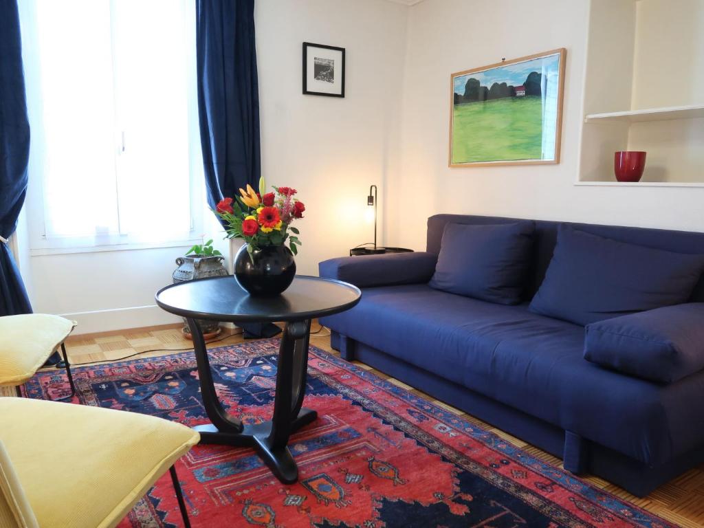 Apartment Petit nid de Pully by Interhome في كولي: غرفة معيشة مع أريكة زرقاء وطاولة مع زهور