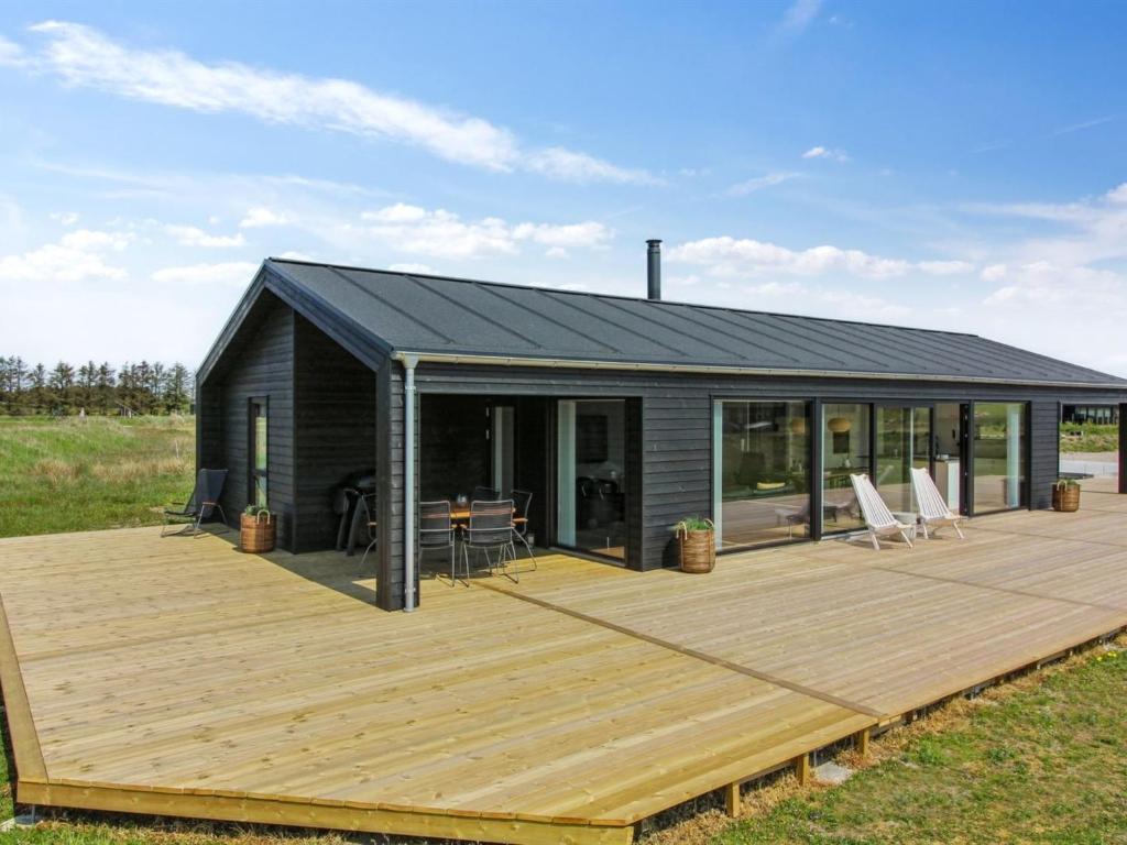 eine schwarze Hütte mit einer Holzterrasse auf einem Feld in der Unterkunft Holiday Home Serey - 1-4km from the sea in NW Jutland by Interhome in Løkken
