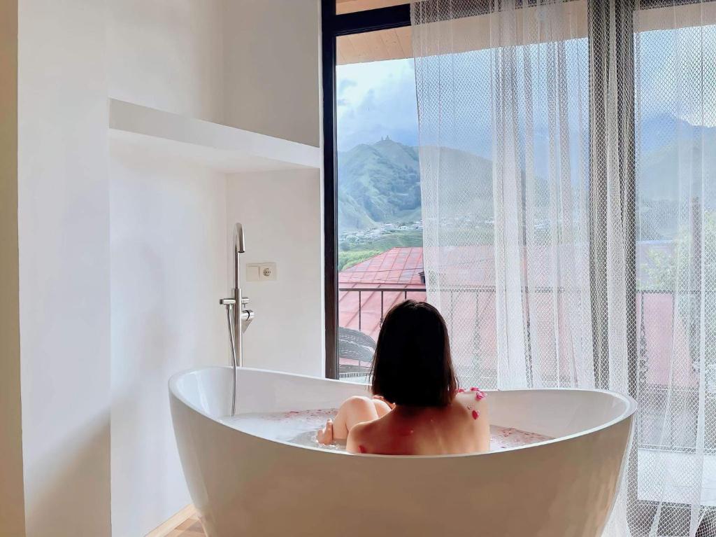 a woman sitting in a bath tub looking out a window at Sunny guesthouse in Stepantsminda