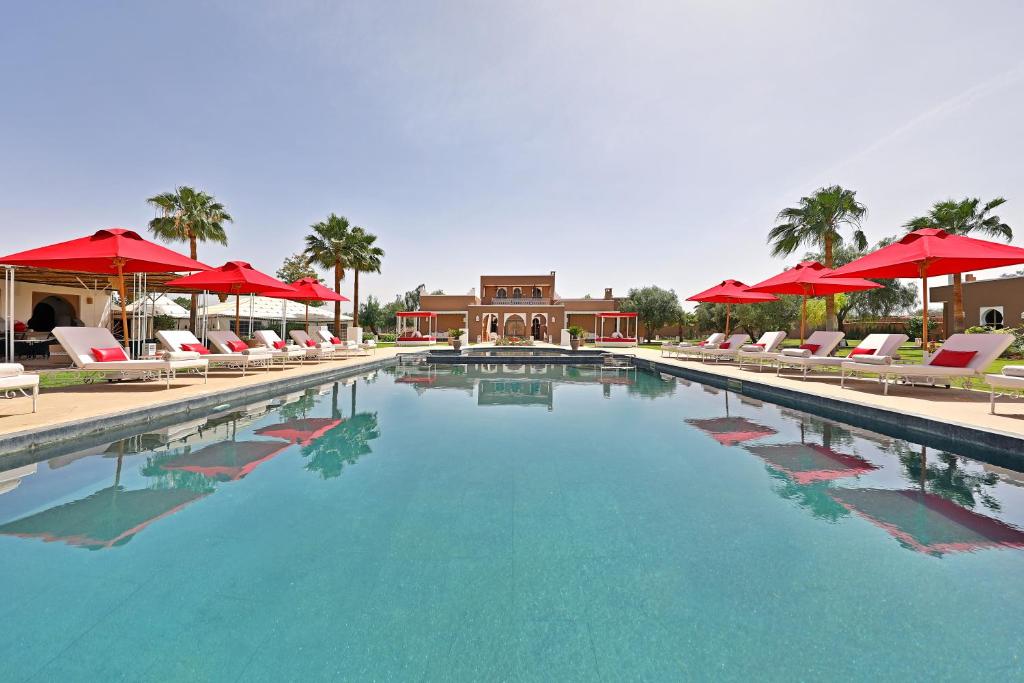 a large swimming pool with red umbrellas and chairs at DOMAINE DU DOUAR in Marrakech