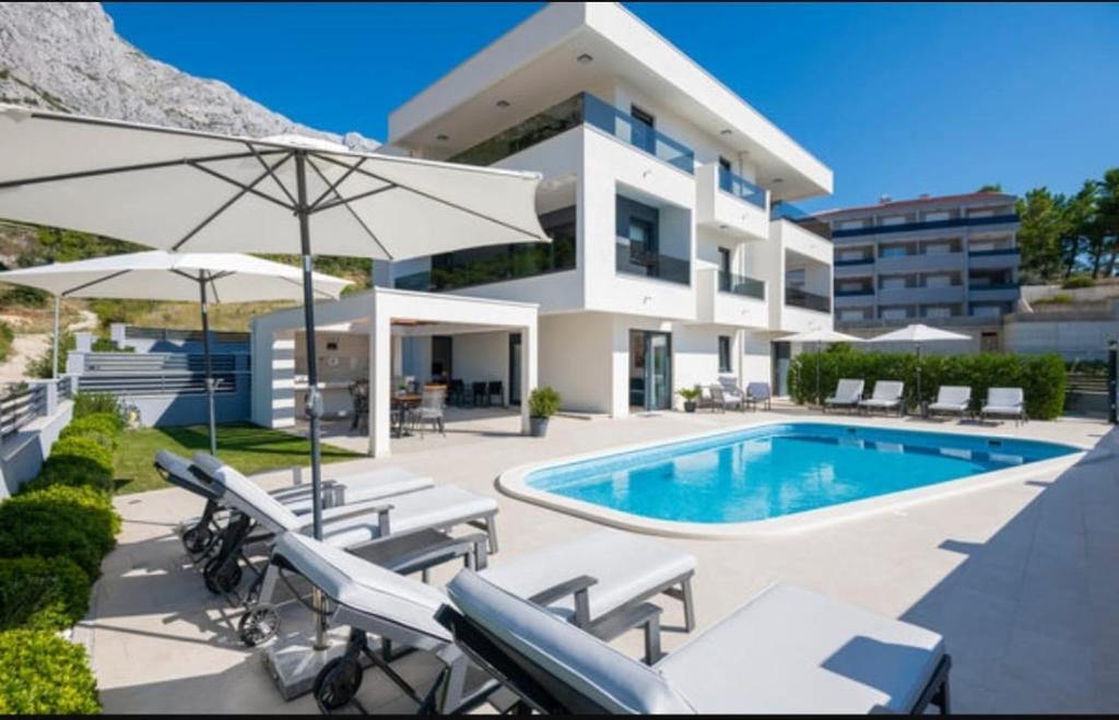 een huis met een zwembad en enkele stoelen en een parasol bij Villa La Vita in Baška Voda