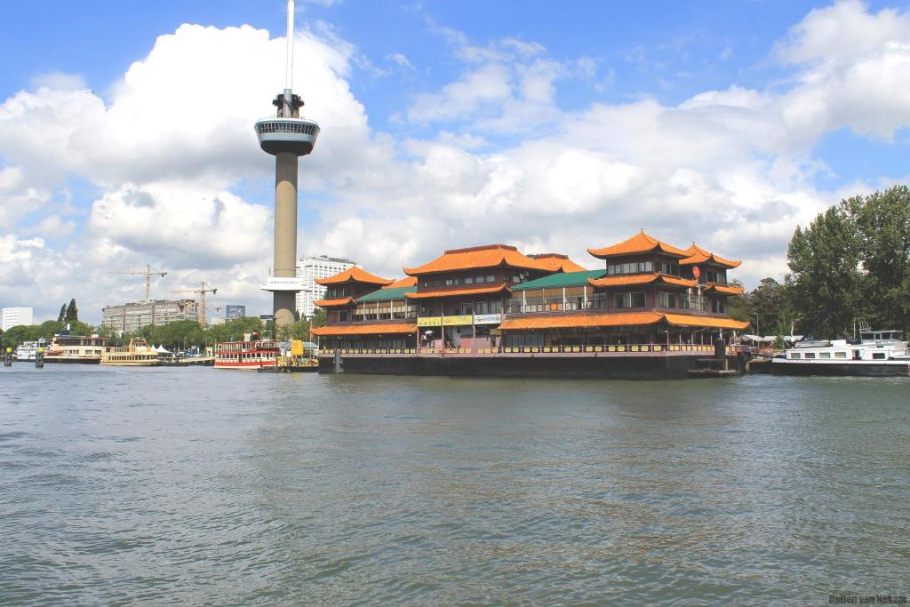 een gebouw op het water met een toren op de achtergrond bij New Ocean Paradise Hotel in Rotterdam