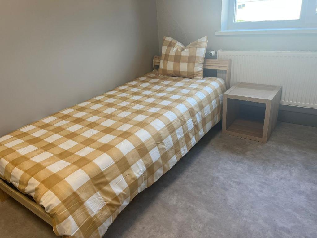 a small bed with a plaid blanket and a night stand at Worker hotel ALEJPARKS in Valmiera