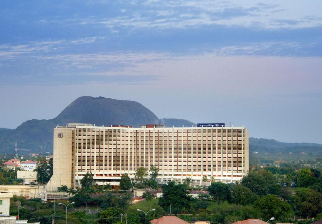 a large white building with a mountain in the background at Transcorp Hilton Abuja in Abuja