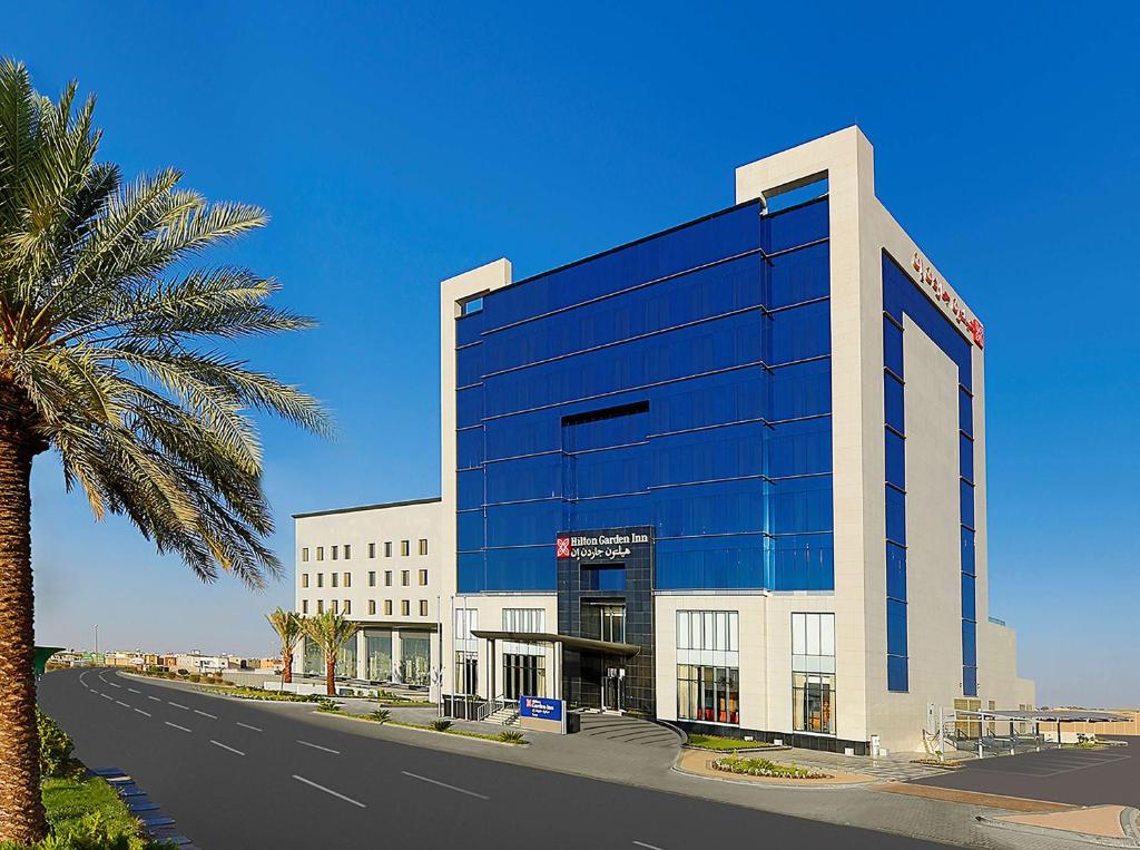 a large building with a palm tree in front of it at Hilton Garden Inn Tabuk in Tabuk