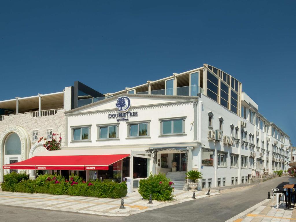 DoubleTree by Hilton Bodrum Marina Vista في بودروم: مبنى أبيض كبير مع مظلة حمراء