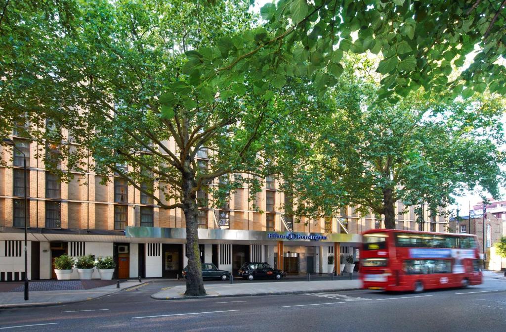 un bus rouge circulant dans une rue en face d'un bâtiment dans l'établissement Hilton London Kensington Hotel, à Londres