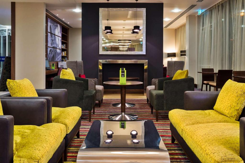 a waiting room with yellow couches and a table at Hampton by Hilton Luton Airport in Luton