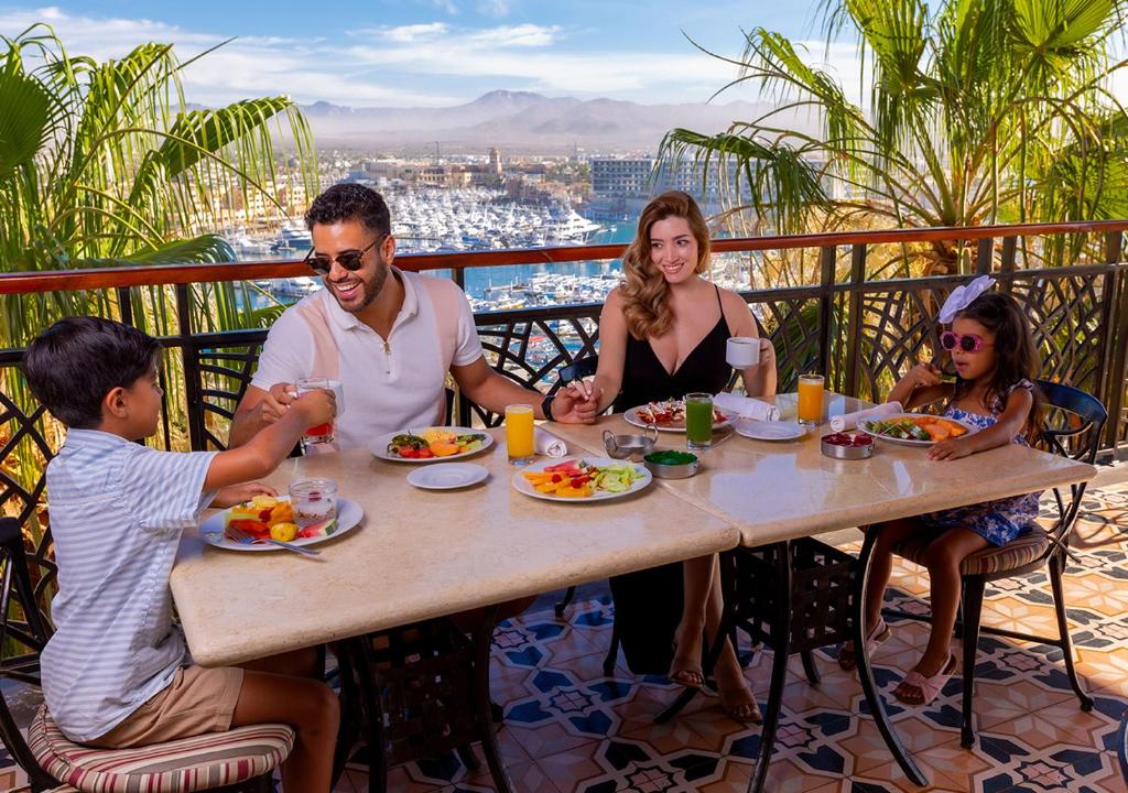 Family dining on balcony with city and marina views, fruit plates and beverages.