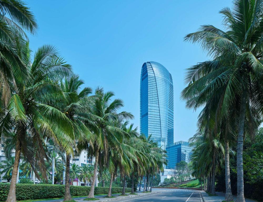 a row of palm trees in front of a tall building at Hilton Haikou in Haikou