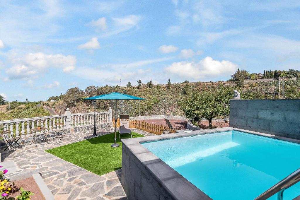a swimming pool with an umbrella on a patio at Raíces Vivas Vivienda Vacacional in Vega de San Mateo