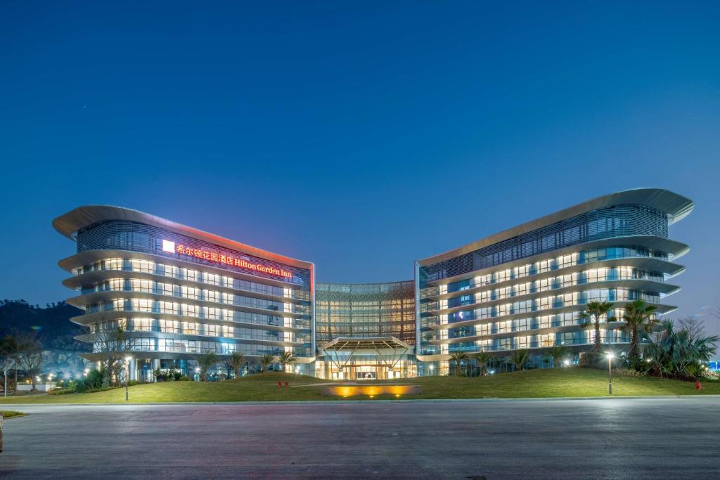 un gran edificio de oficinas con un estacionamiento delante de él en Hilton Garden Inn Zhuhai Hengqin Sumlodol Park en Zhuhai