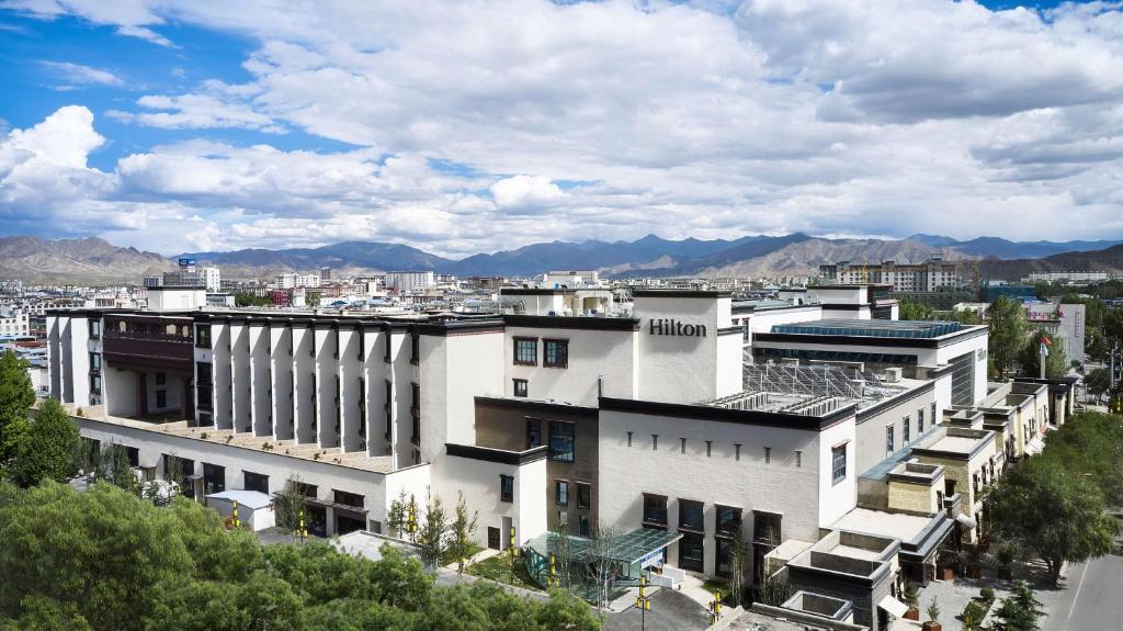 Un grand bâtiment blanc avec des montagnes en arrière-plan dans l'établissement Hilton Shigatse, à Shigatsé