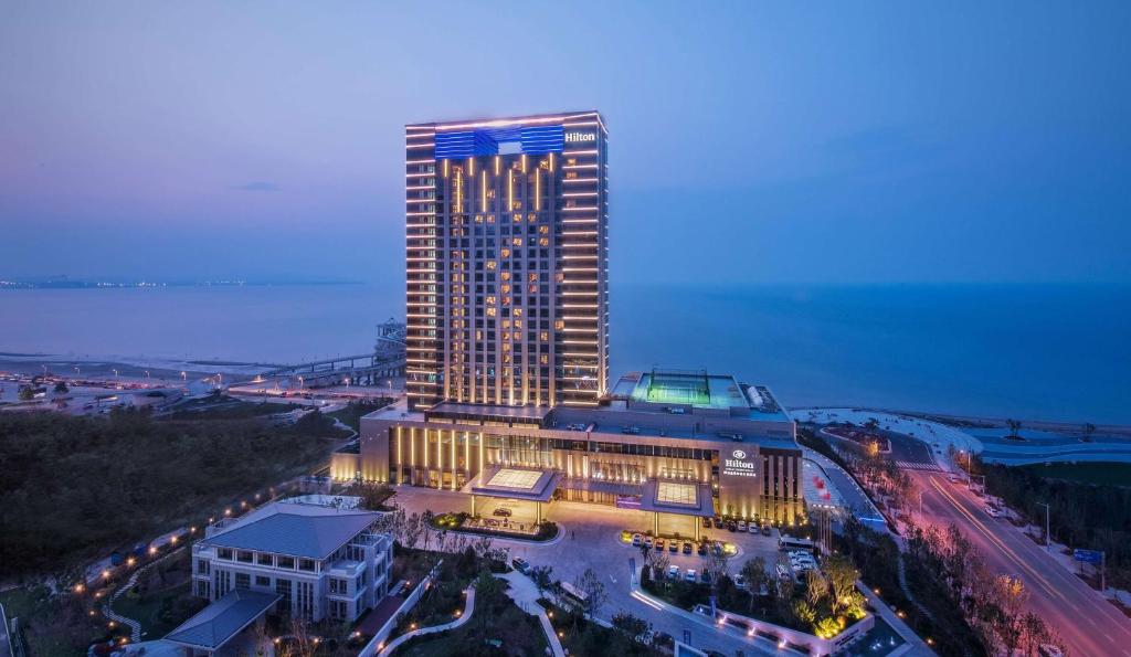 um edifício alto com luzes acesas à noite em Hilton Yantai Golden Coast em Yantai