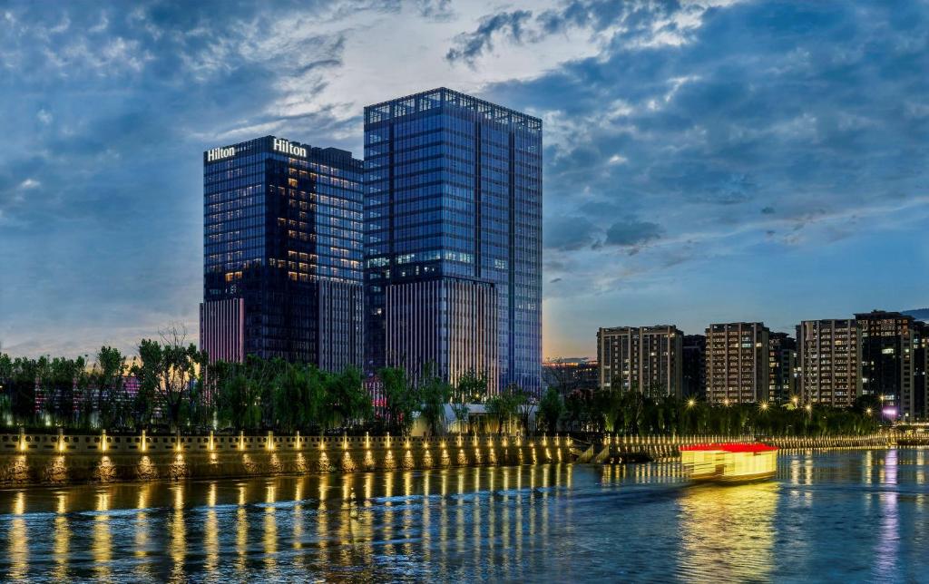 a city skyline with a tall building next to the water at Hilton Yancheng in Yancheng