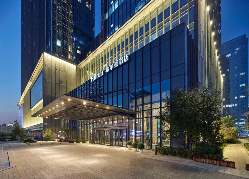 a large glass building with a parking lot in front of it at Hilton Beijing Tongzhou in Beijing