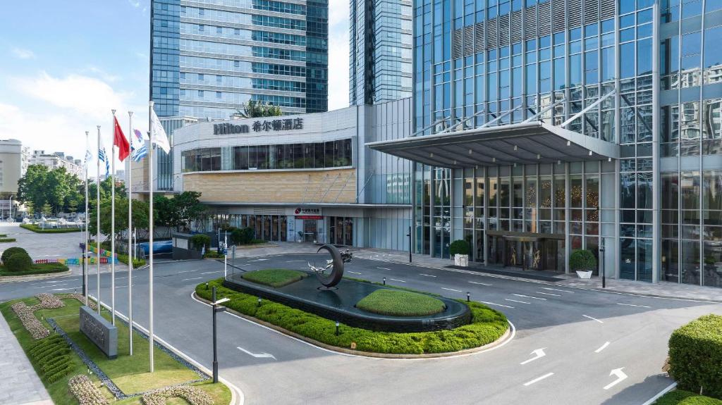 Hilton Foshan Shunde - Free Canton Fair Shuttle Bus في شوند: مبنى فيه تمثال في وسط شارع