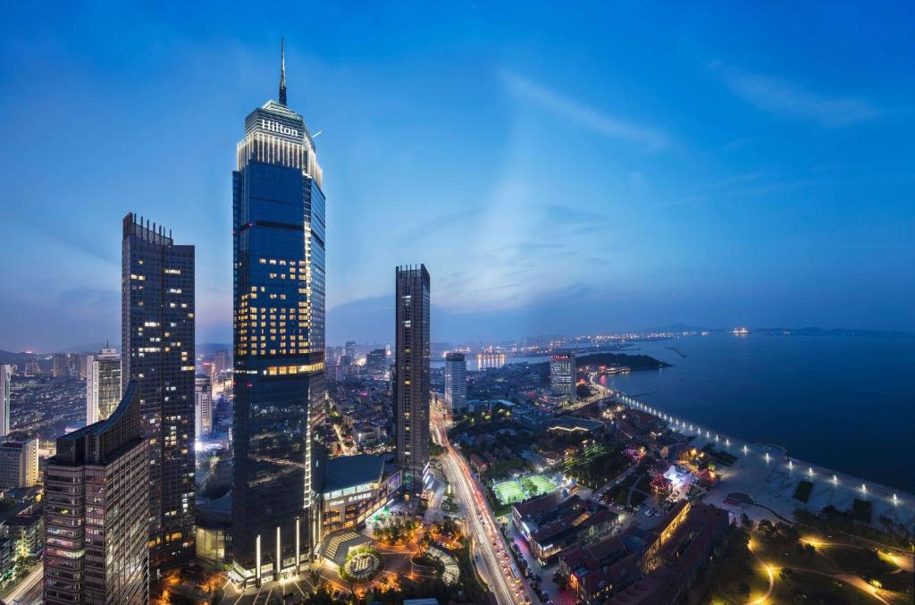 een skyline van de stad 's nachts met een hoog gebouw bij Hilton Yantai in Yantai