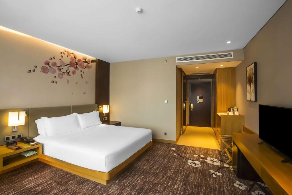 a bedroom with a large white bed and a flat screen tv at Hilton Garden Inn Guiyang Yunyan in Guiyang