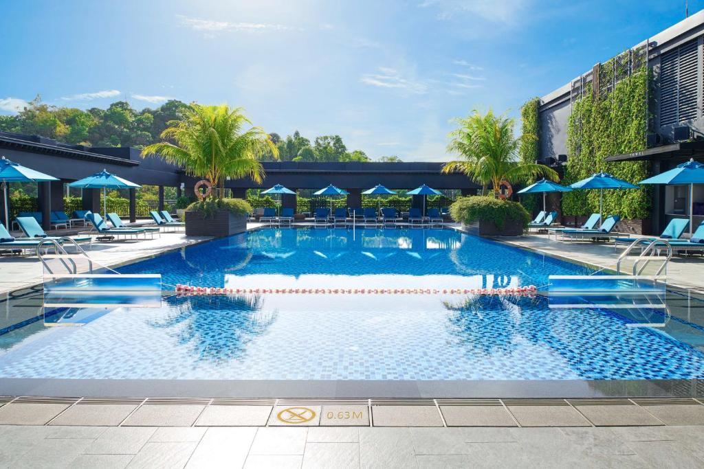 een groot zwembad met blauwe parasols en stoelen bij Hilton Kota Kinabalu in Kota Kinabalu