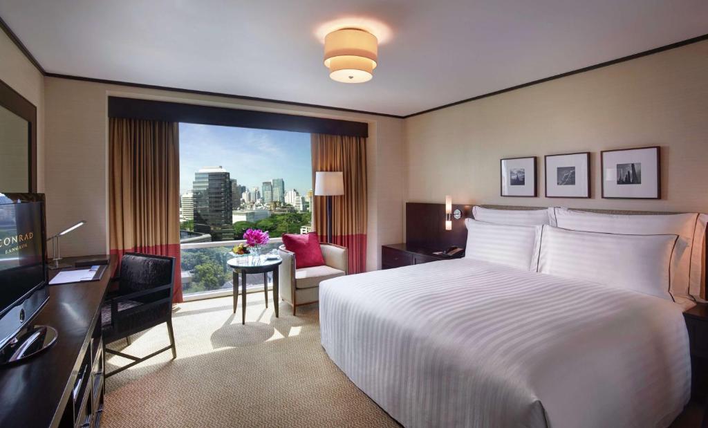 a hotel room with a bed and a desk and a window at Conrad Bangkok Residences in Bangkok