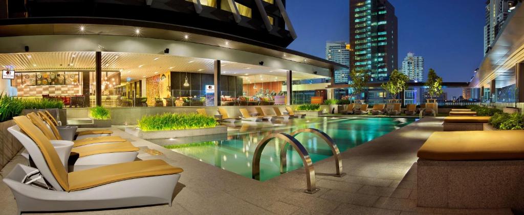 een gebouw met een zwembad en stoelen en gebouwen bij DoubleTree by Hilton Sukhumvit Bangkok in Bangkok