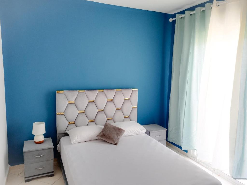 um quarto azul com uma cama branca e uma parede azul em Appartement sur la route de la plage de Achakar em Tânger