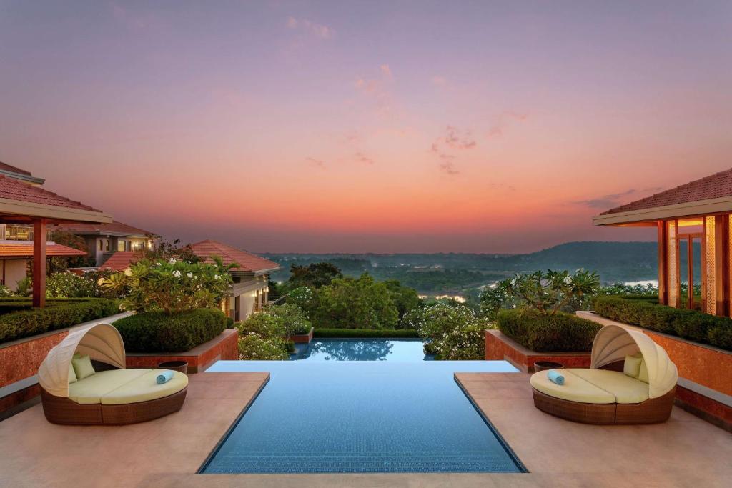 a swimming pool in a villa with a sunset in the background at Hilton Goa Resort Candolim in Candolim