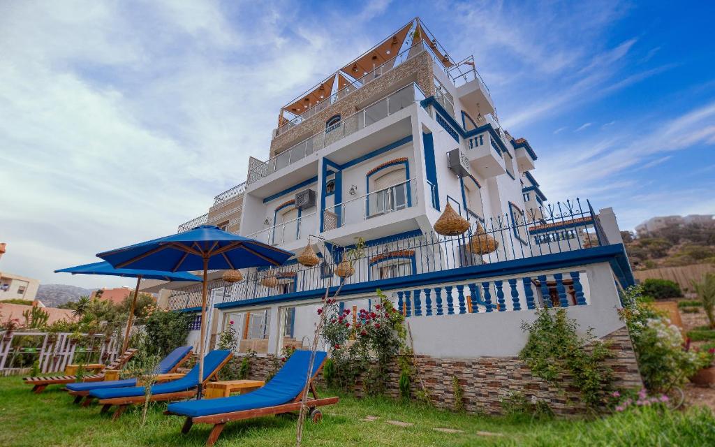 Agadir nʼ Aït Sa的住宿－BLUE WAVE LODGE，前面有椅子和遮阳伞的建筑