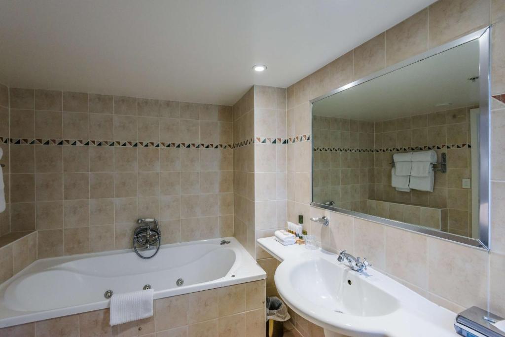 a bathroom with a tub and a sink and a mirror at Chateau On The Park - Christchurch, A Doubletree By Hilton in Christchurch