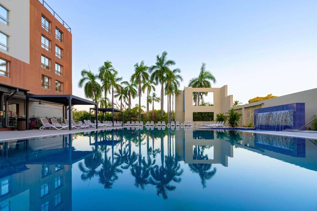 a swimming pool with palm trees and a building at DoubleTree by Hilton Esplanade Darwin in Darwin