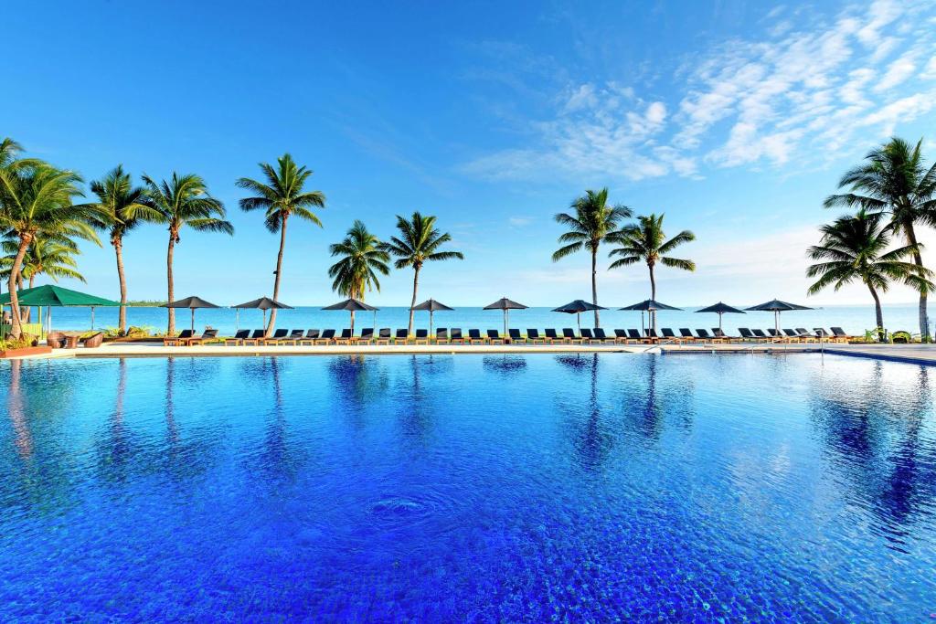 a resort swimming pool with palm trees and umbrellas at Hilton Fiji Beach Resort and Spa in Denarau