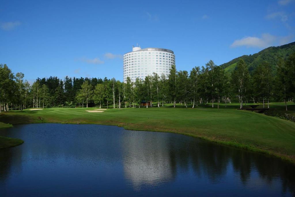 新雪谷的住宿－北海道新雪谷希爾頓度假酒店，一座高尔夫球场,旁边是一座大楼,设有池塘