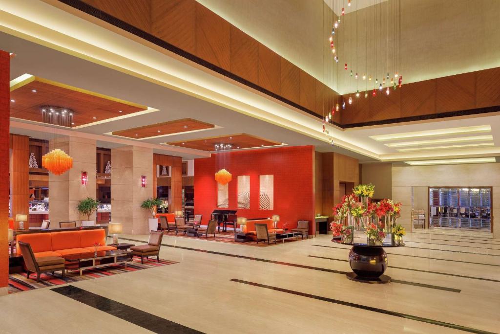 a lobby with a waiting area with orange chairs and flowers at DoubleTree by Hilton Gurgaon New Delhi NCR in Gurgaon