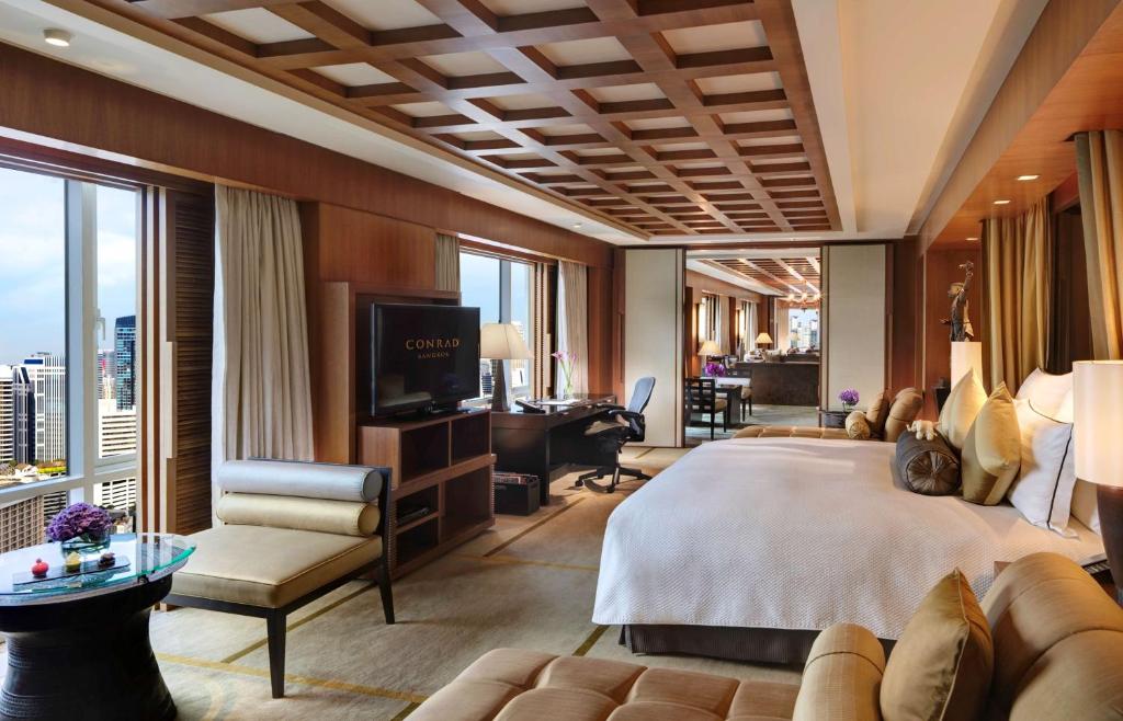 a bedroom with a large bed and a living room at Conrad Bangkok in Bangkok