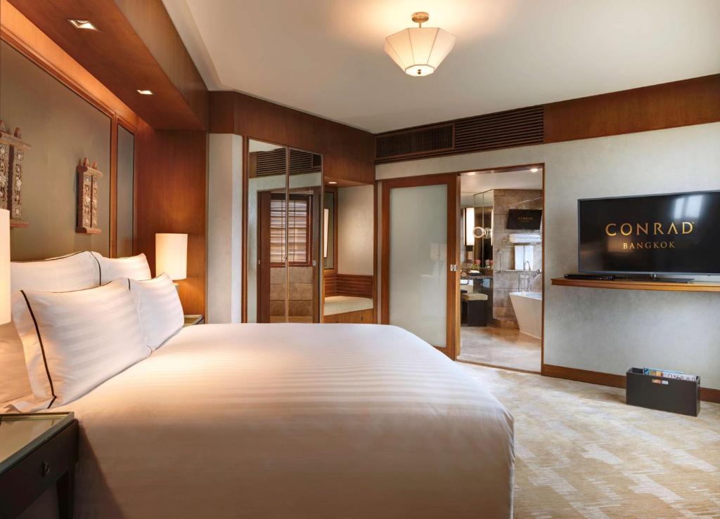 a hotel room with a large bed and a television at Conrad Bangkok in Bangkok