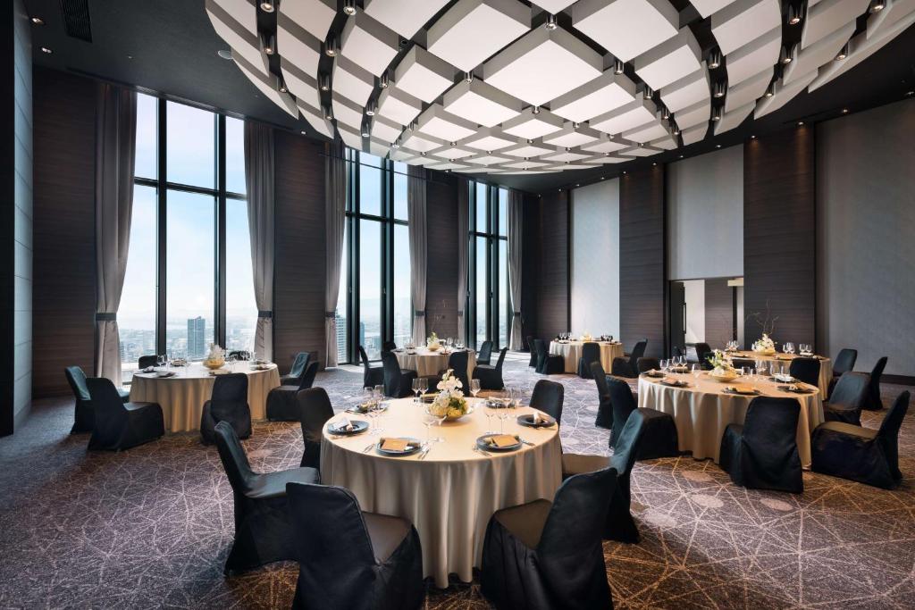 a dining room with tables and chairs and large windows at Conrad Osaka in Osaka