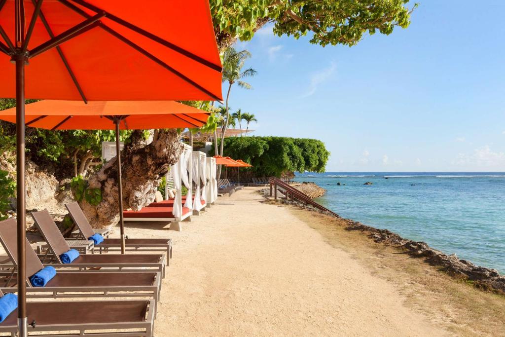 uma praia com cadeiras e guarda-sóis e o oceano em Hilton Guam Resort & Spa em Tumon