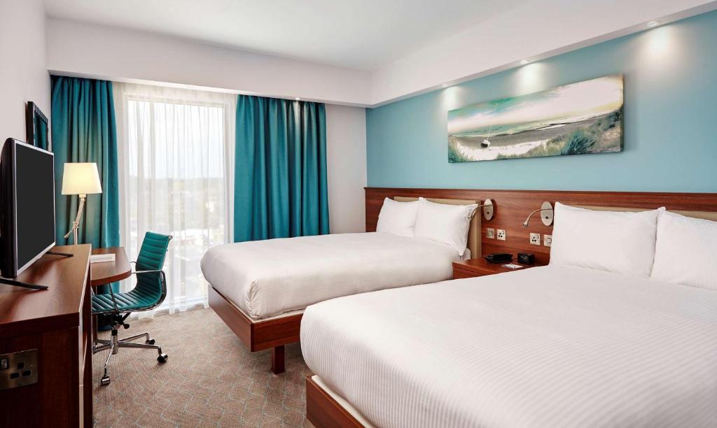 a hotel room with two beds and a desk and a television at Hampton by Hilton Bournemouth in Bournemouth