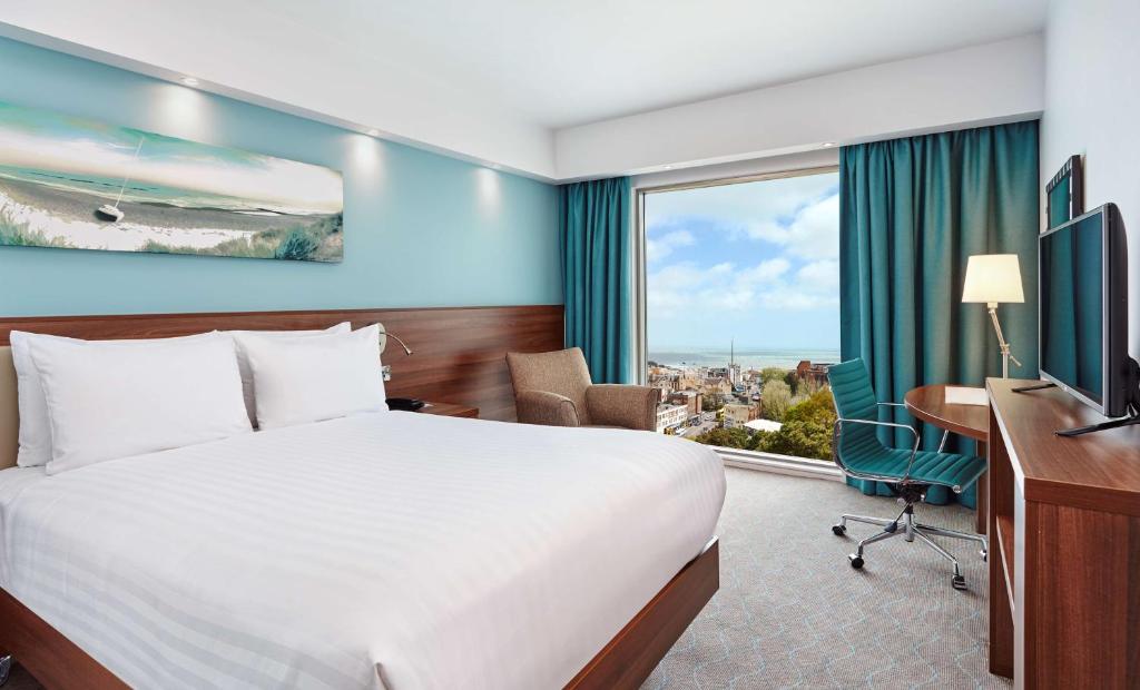 a hotel room with a bed and a desk and a window at Hampton by Hilton Bournemouth in Bournemouth